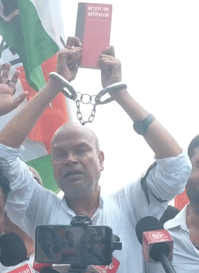 कांग्रेस प्रदेश अध्यक्ष राजेश राम हाथों में हथकड़ी लगाकर संविधान की किताब लेकर प्रदर्शन में शामिल हुए।