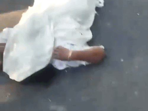 सड़क पर पड़ी महिला की लाश और पास में बैठे लोग।
