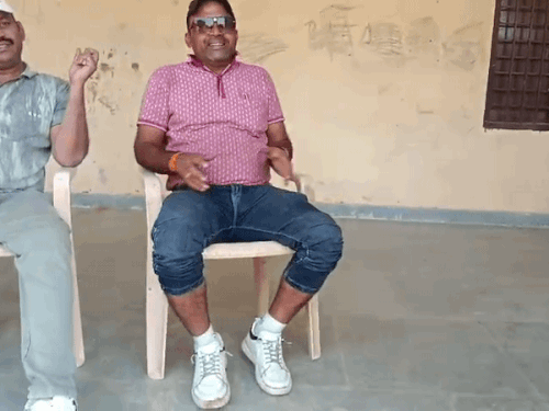 स्कूल कैंपस में क्लासरूम के बाहर जींस घुटनों तक ऊपर किए बैठा टीचर।